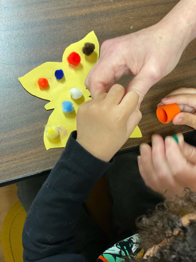 Child putting pom poms on butterfly craft at story time.