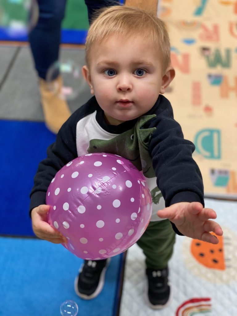 Child catching bubbles while holding a ball during story time.