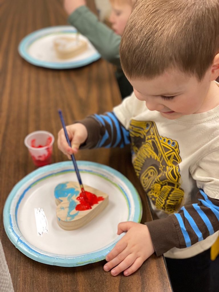 Child painting wooden heart during story time.