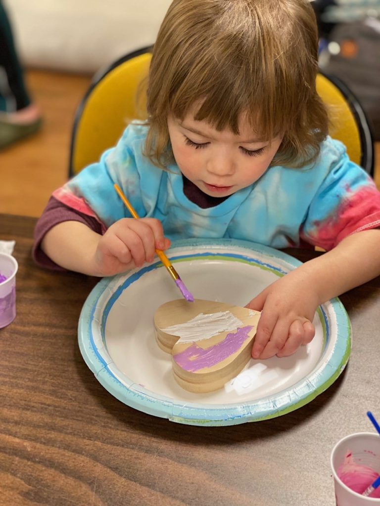 Child painting a wooden heart during story time.